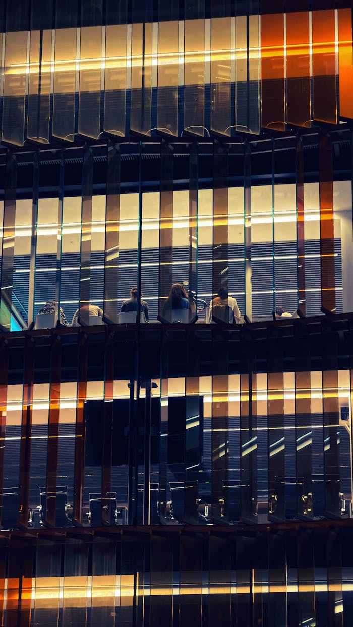 Exterior view of a modern office building in Barcelona, showcasing glass facade and interior lights at night.